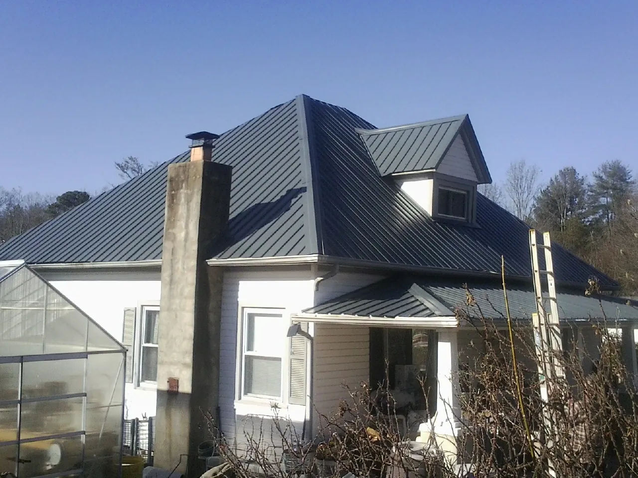 Dark blue standing seam metal roof on a white farmhouse with dormer — Slate & Tile Roof Repair by Roofing Brothers in Hixson