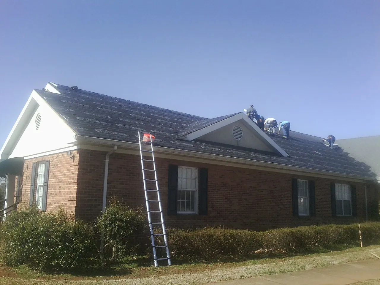 Crew tearing shingles off a brick ranch roof with a ladder set — Emergency Roof Repair work by our crew in Hixson