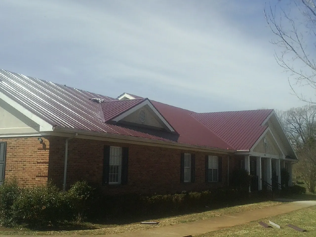 Red metal roof with gabled entries on a long brick building, from a Hail Damage Roof Repair job in Hixson