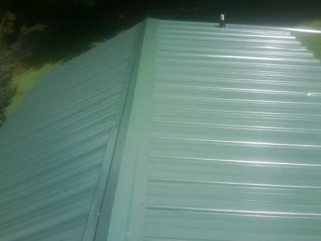 New green metal panels meeting at the ridge of a roof — Flat Roof Repair work by our crew in Hixson