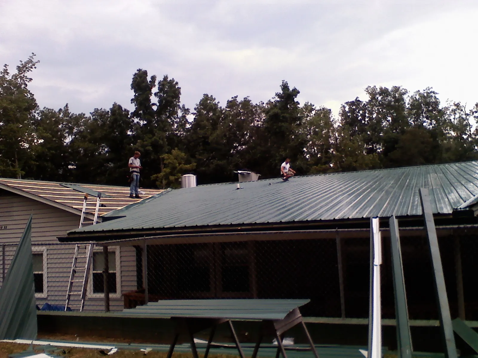 Two roofers installing green metal panels above a covered porch in Hixson