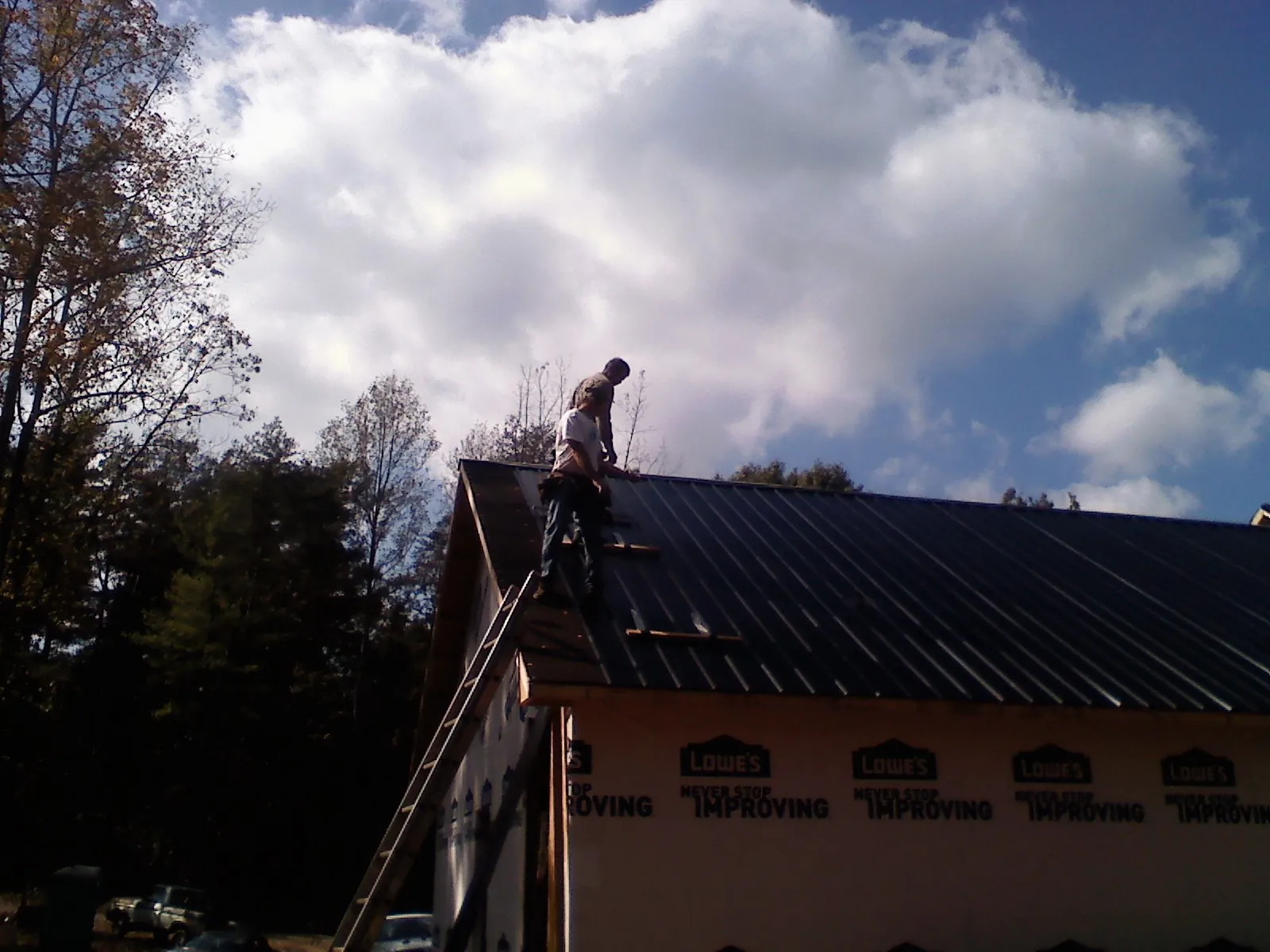 Roofer fastening dark metal panels high against a cloudy sky, from a Roof Inspection job in Hixson