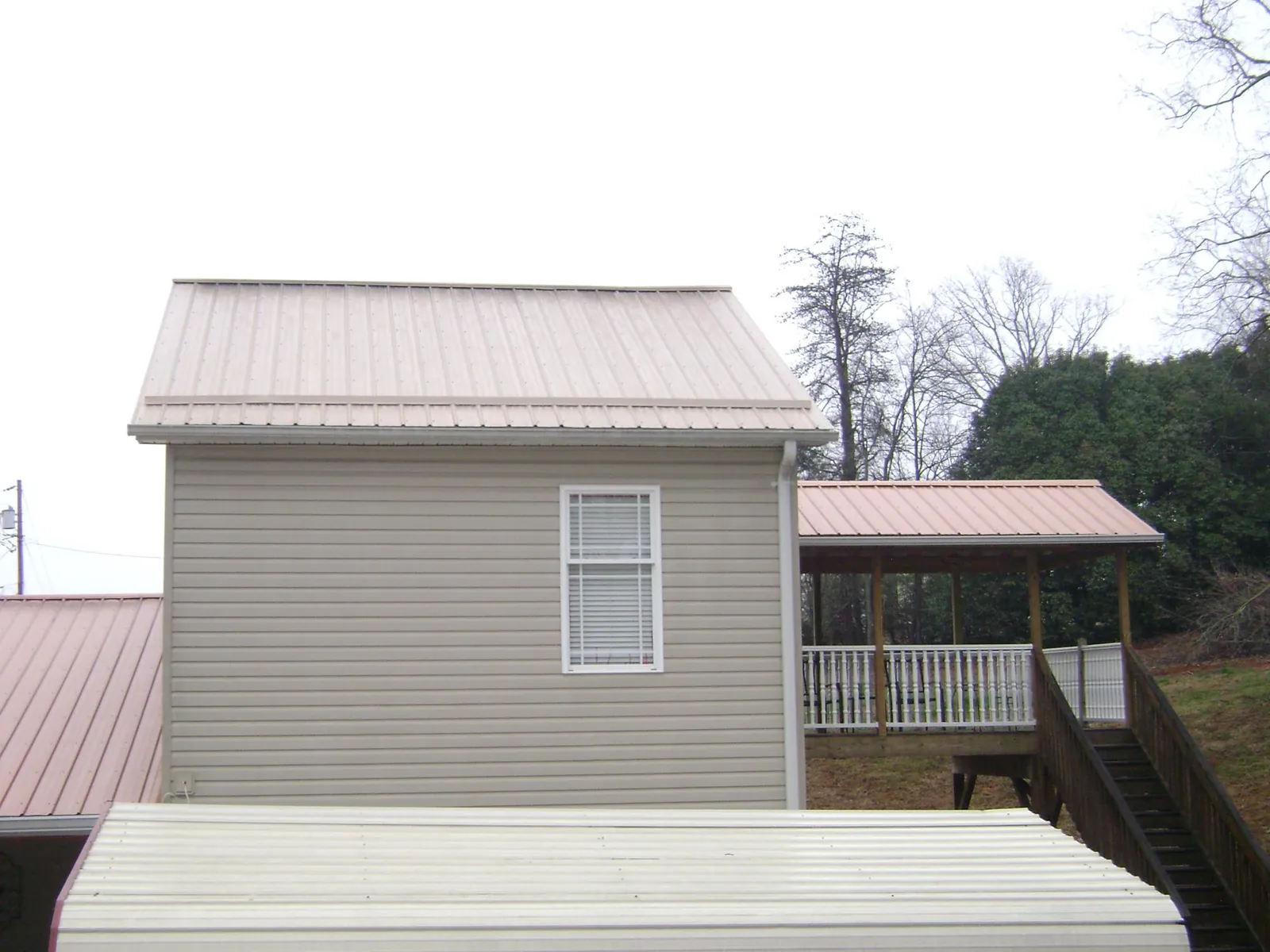 Tan metal roofs on a two story addition and attached porch, from a Roof Replacement job in Hixson